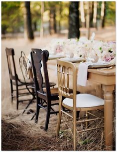 the table is set with white and pink flowers on it, along with black chairs