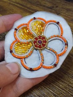 a hand holding a rock with beaded flowers on it and beads in the middle