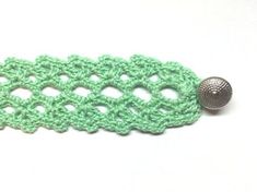 a green crocheted piece with a button on it's end, sitting on a white surface