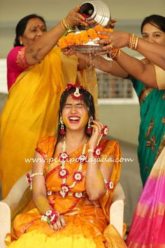 two women in sari are getting their faces painted with yellow and orange colors while one woman is holding a plate