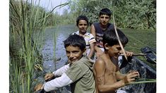 four young boys are standing on a boat in the water and one boy is holding a stick