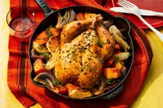 a roasted chicken in a skillet with vegetables and sauce on the side next to a glass of red wine