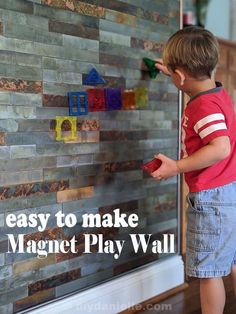 a young boy is playing with magnets on the magnetic play wall that he made