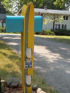 a yellow surfboard sticking out of the ground in front of a mailbox with shoes on it