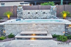 an outdoor hot tub surrounded by stone walls and plants with lights on the steps leading up to it