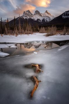 the sun is setting over a mountain range and reflecting in a frozen lake with snow on the ground