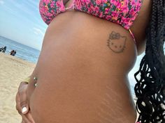 a woman's stomach with a hello kitty tattoo on her belly and the ocean in the background