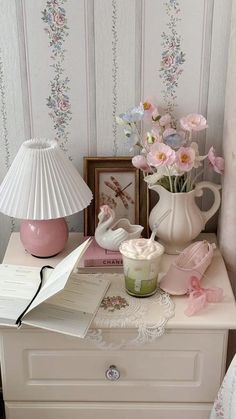 a white dresser topped with pink flowers next to a lamp and a vase filled with flowers