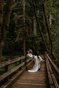 a bride and groom kissing on a bridge in the woods