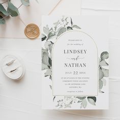 the wedding stationery is laid out on top of a white table with greenery