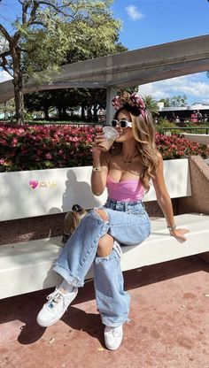 a woman sitting on a white bench drinking from a plastic bottle and wearing ripped jeans