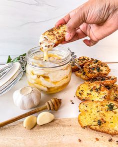 a person dipping something into a jar with garlic bread and garlic on the side next to garlic cloves