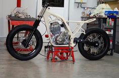 a white motorcycle parked inside of a garage next to a red table with tools on it