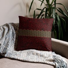 a red and black pillow sitting on top of a couch next to a potted plant