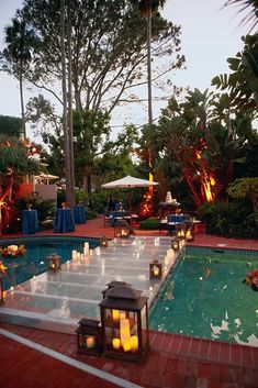 an outdoor dining area with candles and lanterns on the ground next to a swimming pool