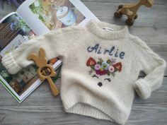 a white sweater with flowers on it next to a pair of scissors and a book