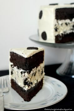 a slice of chocolate cake with white frosting on a plate next to a fork