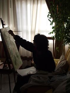 a woman is painting on an easel in her living room with the sun shining through the window