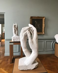 a white sculpture sitting on top of a wooden floor next to a table with a painting on it