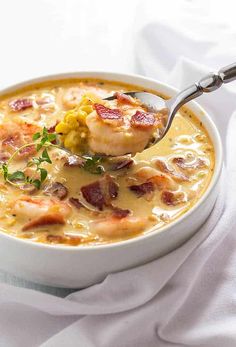 a spoon full of soup with shrimp, corn and bacon in it on a white plate