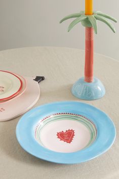 two plates on a table next to a vase with a palm tree in the middle