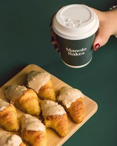 a person holding a cup of coffee next to pastries on a wooden tray with a green background