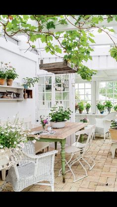 a table and chairs in a room with potted plants on the windowsills