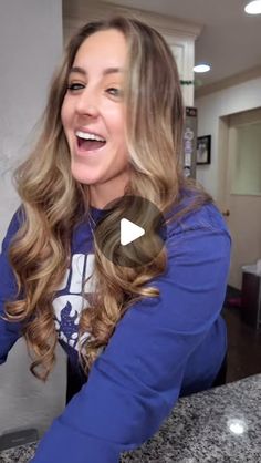 a woman with long hair is smiling at the camera and has her hand on top of a counter