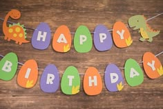 a happy birthday banner with dinosaur decorations on a wooden table next to an orange and green egg