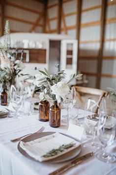 the table is set with white flowers and place settings