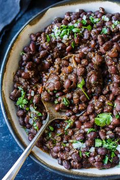 a bowl filled with beans and parsley on top of a blue countertop next to a spoon