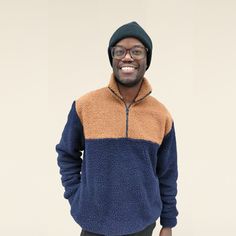 a smiling man in a blue and brown jacket smiles at the camera with his hands in his pockets