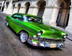 an old green car parked on the side of the road in front of a building