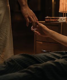 two people reaching out to touch each other's hand on a bed in a dark room