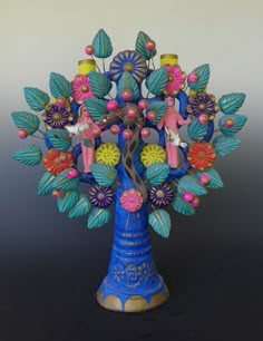 a blue vase filled with lots of colorful flowers and figurines on top of it