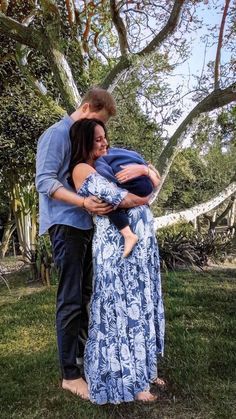 a man and woman embracing each other in the grass under a tree with their arms around one another