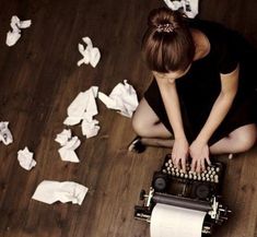 a woman is sitting on the floor next to a typewriter and some toilet paper