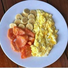 an omelet, scrambled eggs and sliced bananas on a white plate sitting on a wooden table