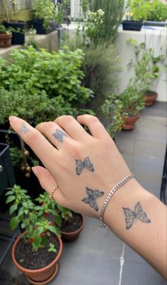 a woman's hand with butterfly tattoos on her left wrist, and potted plants in the background