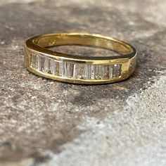 a yellow gold ring with baguets set in the middle on top of a rock