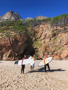 three surfers are walking on the beach with their surfboards in hand and one is carrying his board