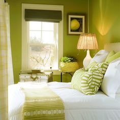 a bedroom with green walls, white bedding and yellow lamps on the windowsill