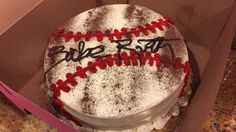 a baseball cake in a box with writing on the top and red, white and black frosting