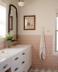 a bathroom with pink and white tile walls, two sinks and a framed painting on the wall