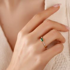 a woman's hand wearing a gold ring with an emerald and white diamond set in the middle