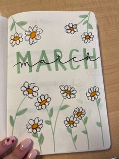 a hand holding an open notebook with flowers on it and the word march written in cursive writing