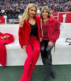 two women in red jackets and black pants posing for a photo at a football game