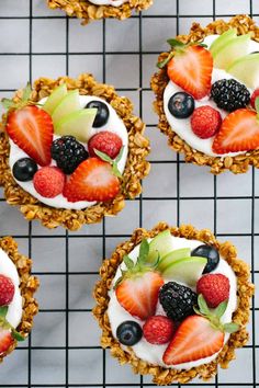 four desserts with strawberries, apples, and blueberries on top are sitting on a cooling rack