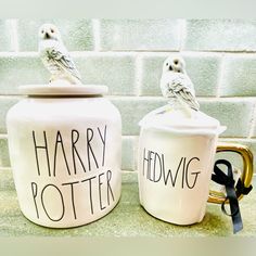 two harry potter mugs with owls sitting on top of them, one is white and the other has black lettering