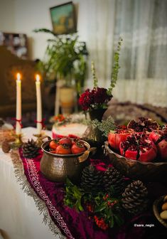 a table topped with bowls filled with fruit next to two lit candles and pine cones